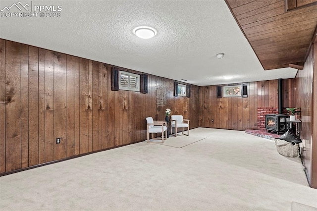 sitting room with wooden walls, a wood stove, carpet flooring, and a textured ceiling