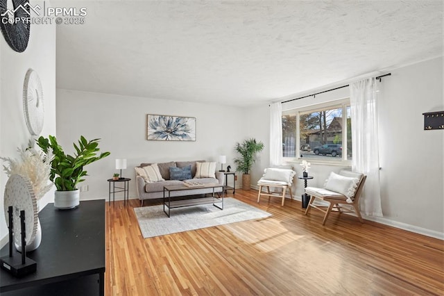 living room with a textured ceiling, baseboards, and wood finished floors
