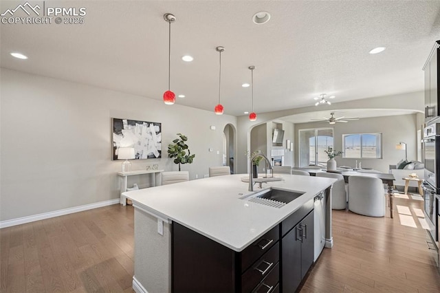 kitchen featuring a ceiling fan, a sink, arched walkways, light wood-style floors, and open floor plan