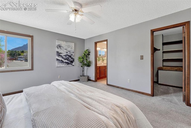 bedroom featuring a ceiling fan, a walk in closet, baseboards, a textured ceiling, and light colored carpet