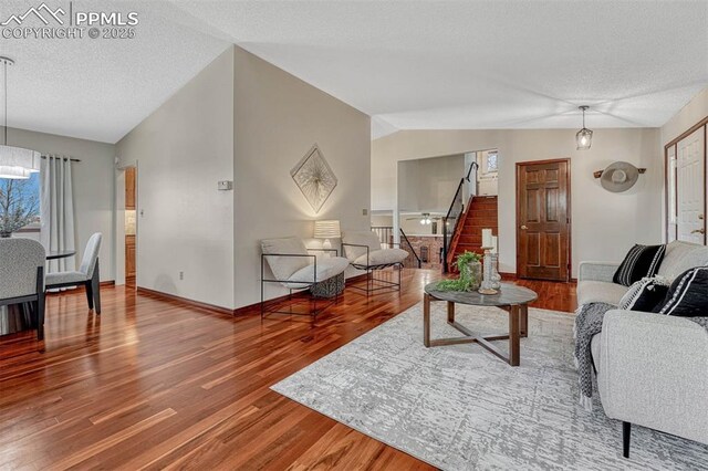 living area featuring stairway, lofted ceiling, wood finished floors, and a textured ceiling