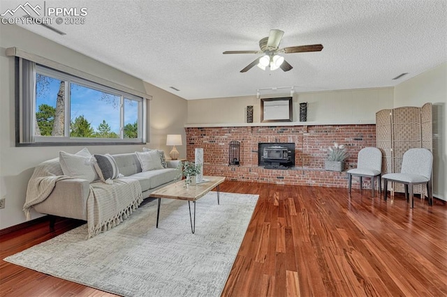 living area featuring a ceiling fan, a wood stove, wood finished floors, and a textured ceiling