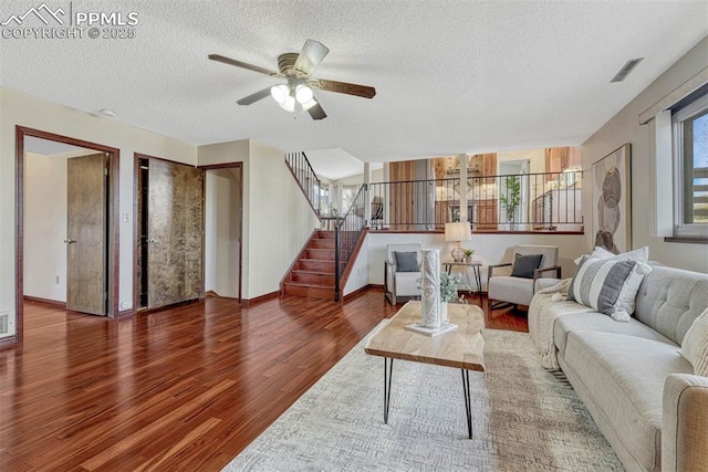 living area featuring a textured ceiling, visible vents, wood finished floors, stairs, and ceiling fan