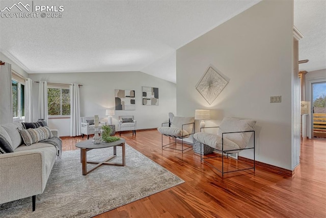 living area with baseboards, vaulted ceiling, wood finished floors, and a textured ceiling