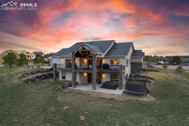 4043 Needles Dr, Colorado Springs, CO 80908 - back of house at dusk with a balcony, stone siding, a patio, stucco siding, and a hot tub
