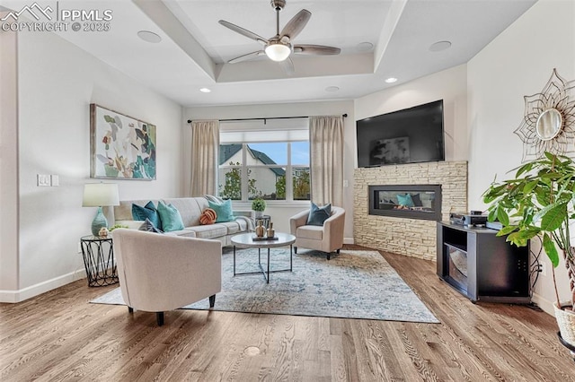 4464 Portillo Pl, Colorado Springs, CO 80924 - living room featuring wood finished floors, a stone fireplace, baseboards, a raised ceiling, and a ceiling fan