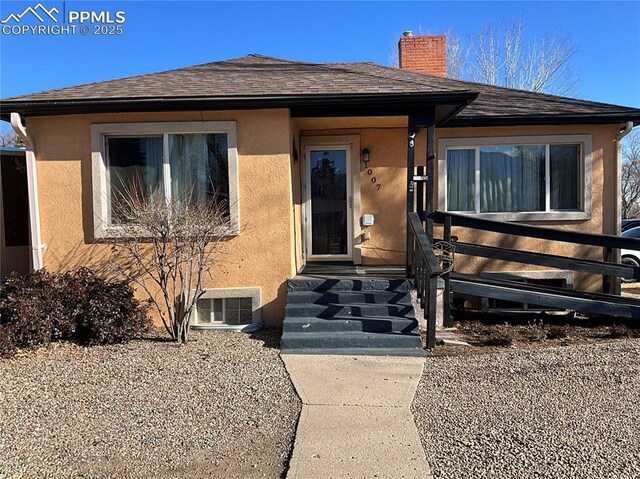 1007 Iowa Ave, Colorado Springs, CO 80909 - view of exterior entry featuring roof with shingles, a chimney, and stucco siding