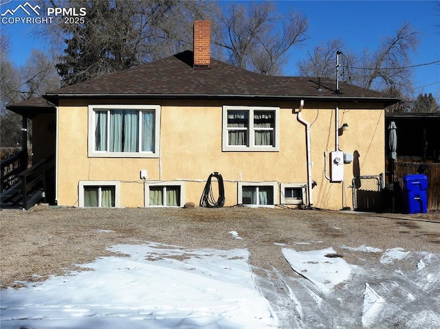 1007 Iowa Ave, Colorado Springs, CO 80909 - snow covered rear of property with a chimney, a shingled roof, and stucco siding