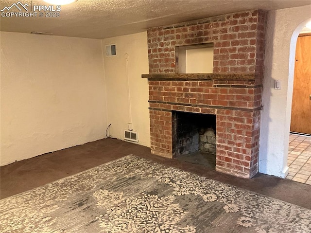 1007 Iowa Ave, Colorado Springs, CO 80909 - unfurnished living room featuring visible vents, a brick fireplace, arched walkways, and a textured ceiling