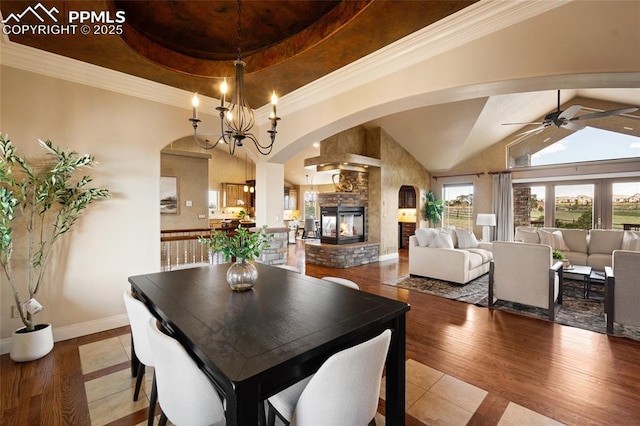 dining area featuring arched walkways, ceiling fan, a multi sided fireplace, baseboards, and a tray ceiling