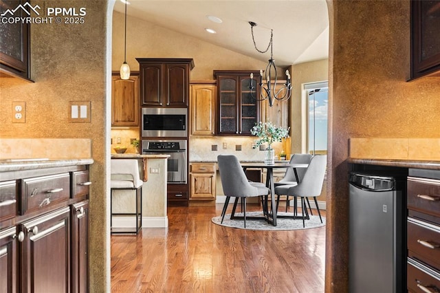 kitchen with appliances with stainless steel finishes, lofted ceiling, light countertops, wood finished floors, and pendant lighting