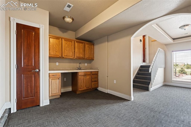 bar area featuring dark colored carpet, baseboards, stairs, a sink, and arched walkways