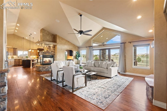 living area featuring dark wood-style floors, a fireplace, baseboards, ceiling fan, and high vaulted ceiling