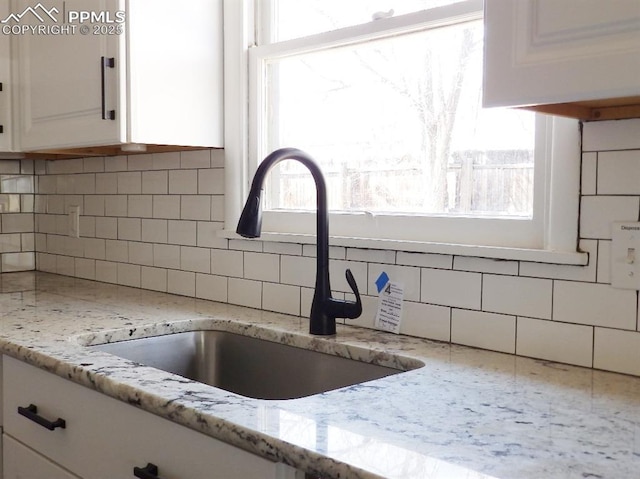 interior details featuring light stone counters, tasteful backsplash, a sink, and white cabinetry