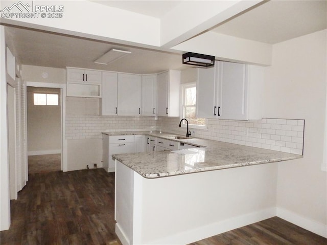 kitchen featuring light stone countertops, dark wood-style flooring, a peninsula, tasteful backsplash, and white cabinetry