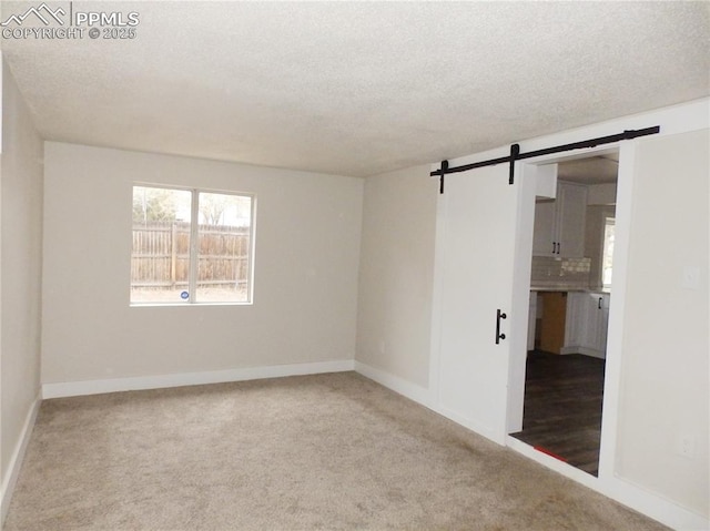 carpeted empty room with baseboards, a textured ceiling, and a barn door