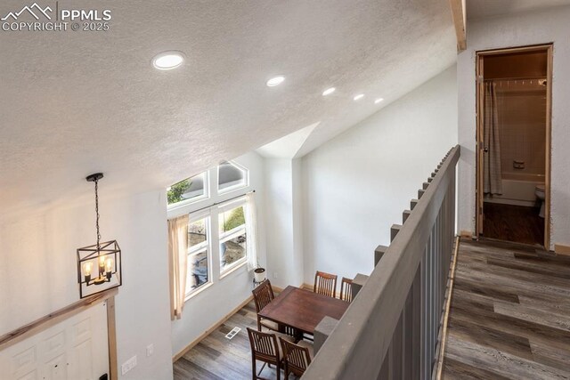 hallway featuring a textured ceiling, an inviting chandelier, dark wood-style floors, and lofted ceiling