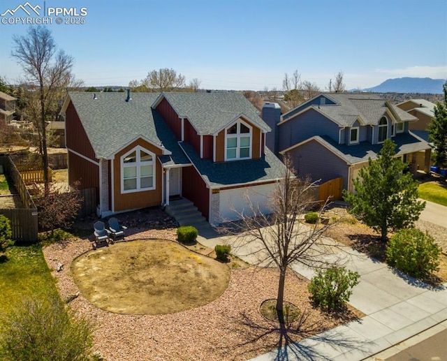 view of front facade featuring driveway, roof with shingles, a garage, fence, and a mountain view