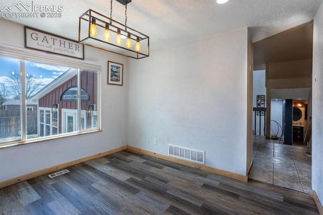 unfurnished dining area with baseboards, a textured ceiling, wood finished floors, and visible vents