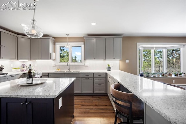 kitchen with plenty of natural light, a sink, gray cabinets, and light stone countertops