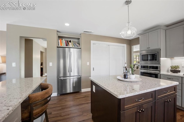 kitchen with dark wood-style flooring, a kitchen bar, visible vents, pendant lighting, and stainless steel appliances