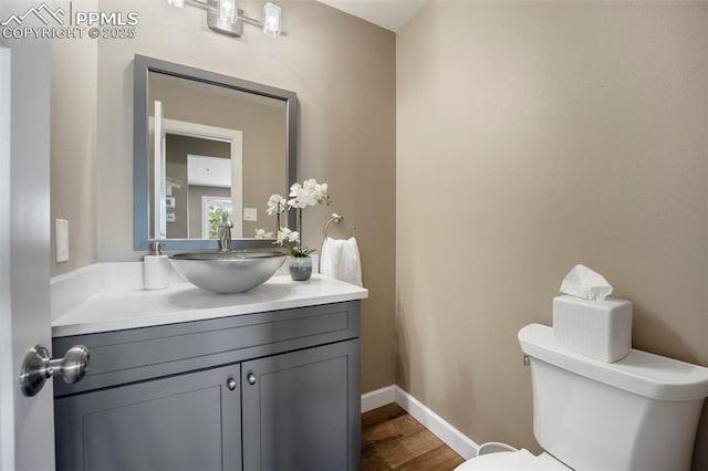 half bath featuring toilet, baseboards, wood finished floors, and vanity
