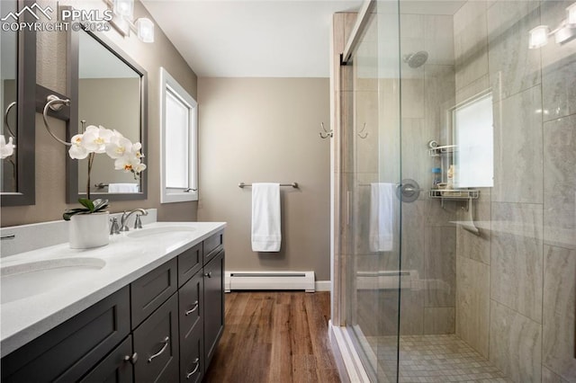 full bathroom featuring a sink, double vanity, a shower stall, wood finished floors, and a baseboard heating unit