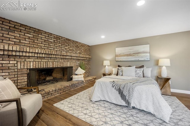 bedroom with recessed lighting, baseboards, a brick fireplace, and wood finished floors