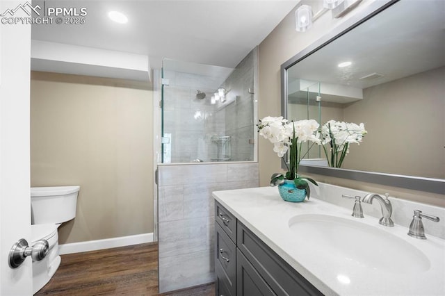 bathroom featuring vanity, wood finished floors, toilet, baseboards, and a tile shower