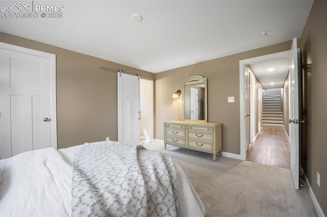 bedroom featuring light colored carpet, a barn door, and baseboards