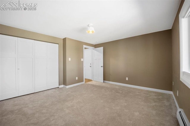 unfurnished bedroom featuring light colored carpet, baseboards, baseboard heating, and a closet
