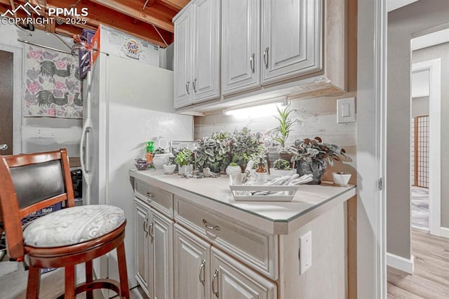 kitchen featuring light wood-style floors, light countertops, freestanding refrigerator, and tasteful backsplash