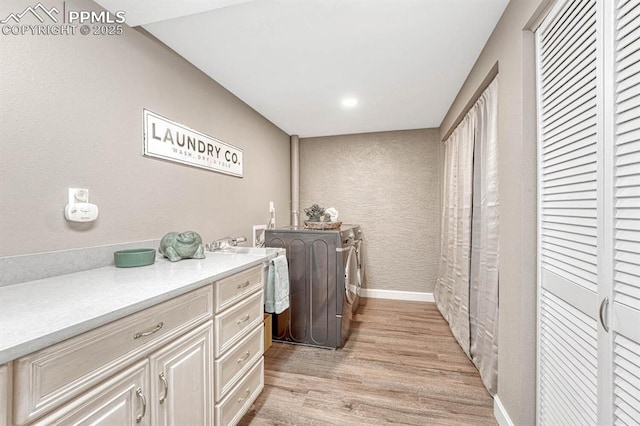 laundry area with a textured wall, baseboards, cabinet space, separate washer and dryer, and light wood-style flooring
