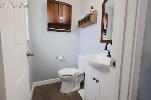half bath featuring baseboards, toilet, vanity, and wood finished floors