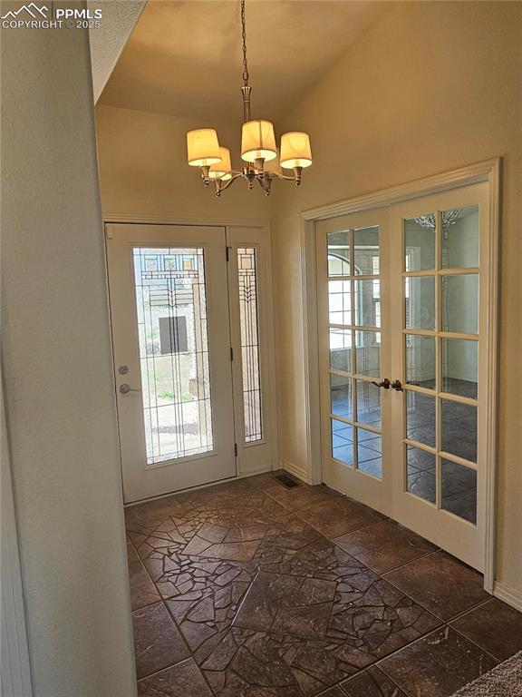 entryway with vaulted ceiling, stone tile floors, an inviting chandelier, french doors, and baseboards
