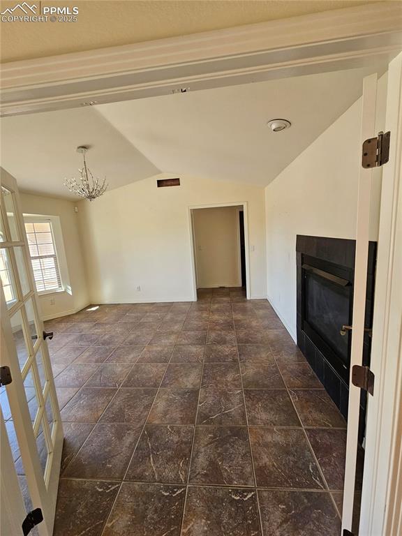 unfurnished living room featuring baseboards, vaulted ceiling, a chandelier, and a fireplace