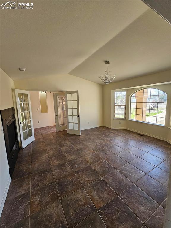 empty room with lofted ceiling, french doors, baseboards, and an inviting chandelier
