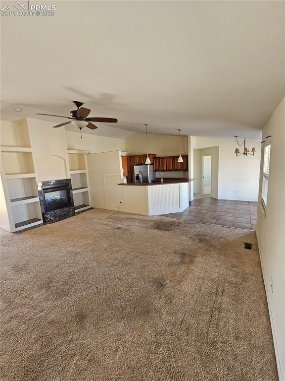 unfurnished living room featuring carpet, lofted ceiling, visible vents, a glass covered fireplace, and ceiling fan