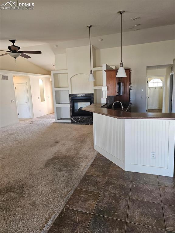 kitchen featuring lofted ceiling, dark countertops, visible vents, a multi sided fireplace, and ceiling fan