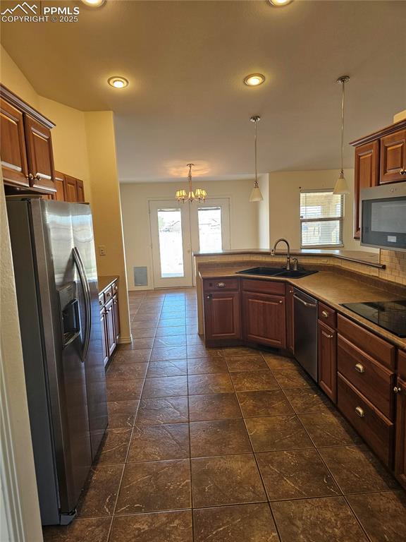 kitchen featuring a sink, pendant lighting, appliances with stainless steel finishes, a peninsula, and a notable chandelier