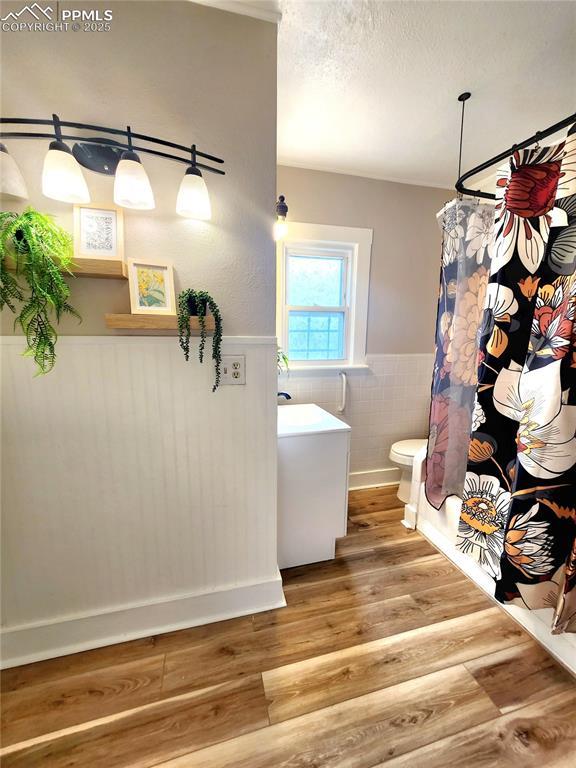 full bathroom with curtained shower, wood finished floors, toilet, and wainscoting
