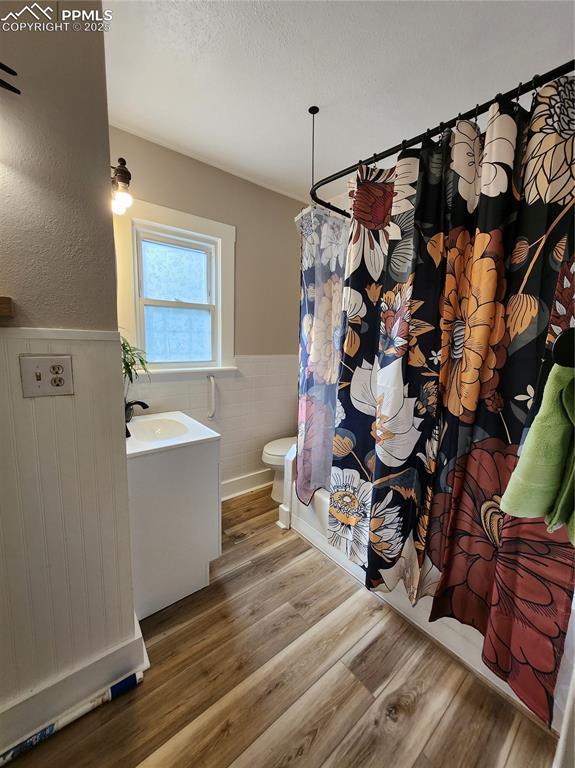 full bathroom featuring a wainscoted wall, toilet, tile walls, wood finished floors, and vanity