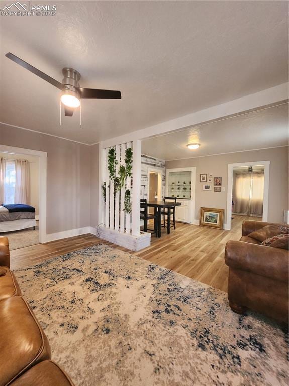 living room with light wood finished floors, a ceiling fan, and baseboards