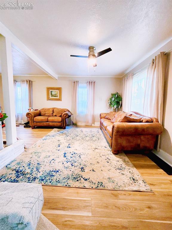 living room with beamed ceiling, plenty of natural light, a ceiling fan, and wood finished floors