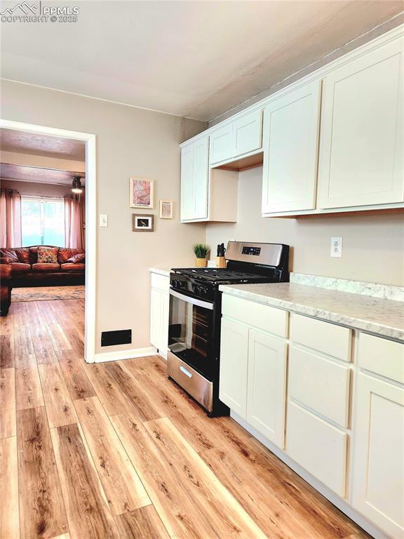 kitchen featuring white cabinets, baseboards, light wood-style floors, and gas range