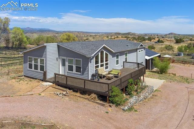 rear view of property featuring a deck with mountain view, driveway, and a shingled roof