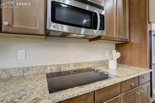 kitchen with stainless steel microwave, black electric stovetop, and light stone countertops