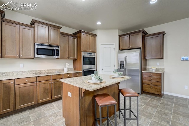 kitchen featuring a center island, a breakfast bar area, baseboards, appliances with stainless steel finishes, and light stone countertops