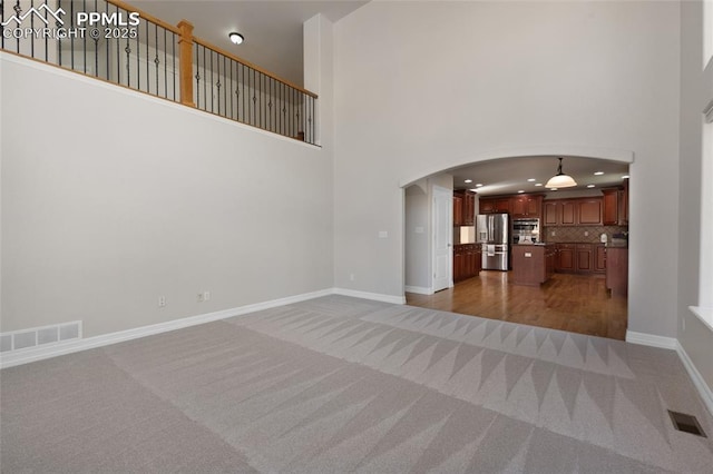 7436 Centennial Glen Dr, Colorado Springs, CO 80919 - unfurnished living room featuring carpet floors, a high ceiling, arched walkways, and visible vents
