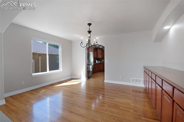 7436 Centennial Glen Dr, Colorado Springs, CO 80919 - unfurnished dining area with arched walkways, baseboards, light wood finished floors, and a chandelier